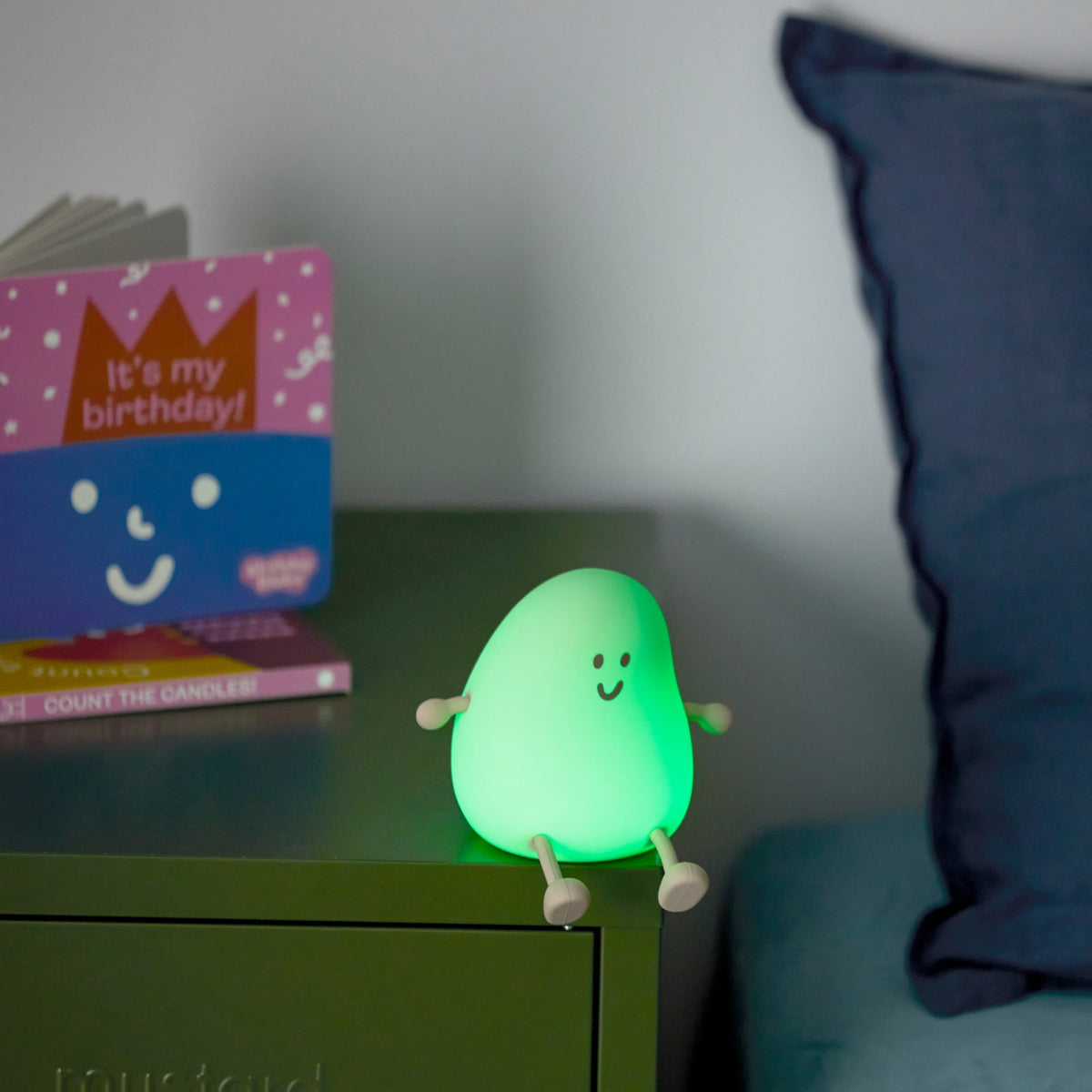 Green night light on a bedside table with a book and pillow in the background