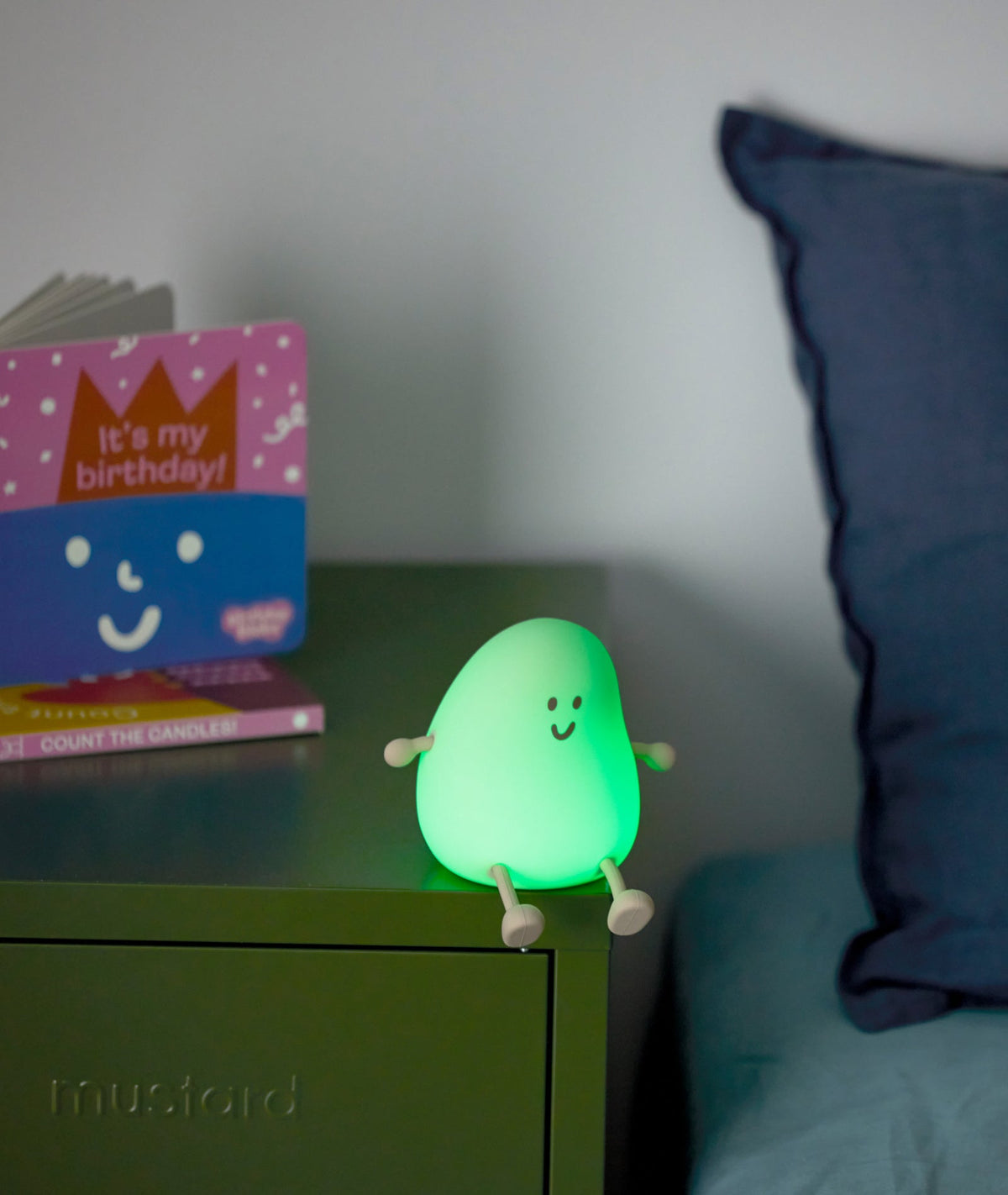 Green night light on a bedside table with a book and pillow in the background