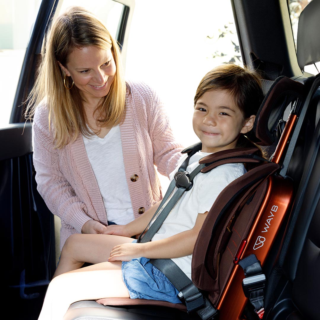 Woman adjusting a child's car seat in a vehicle, with a visible brand logo.