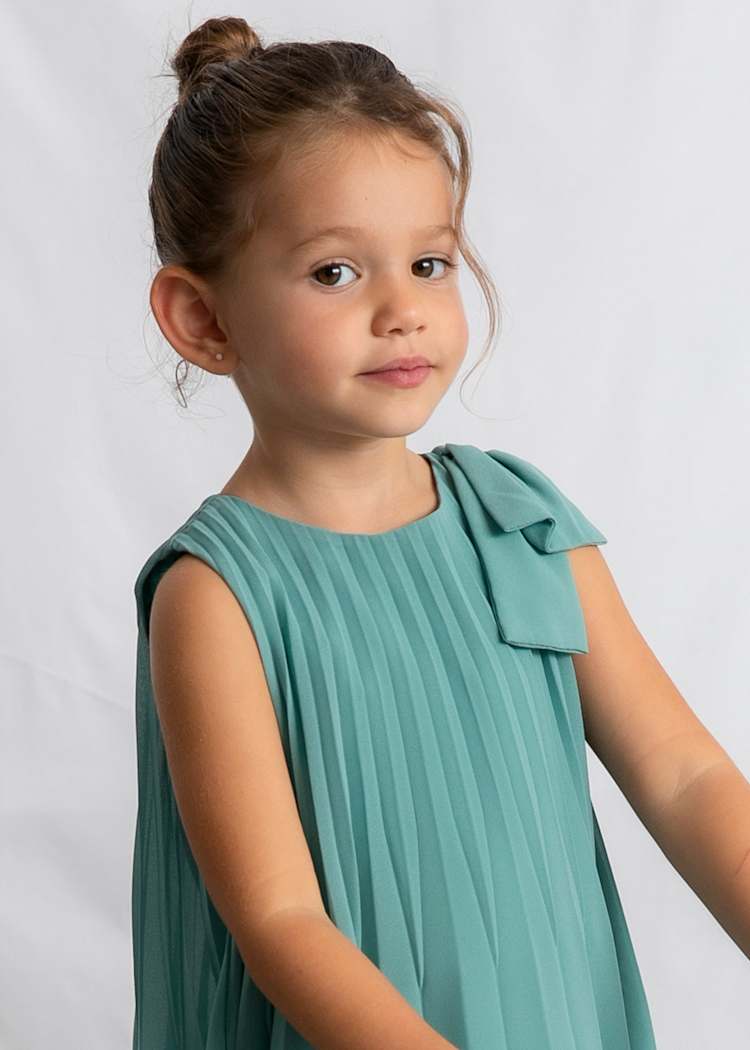 Young girl wearing a teal dress against a plain background
