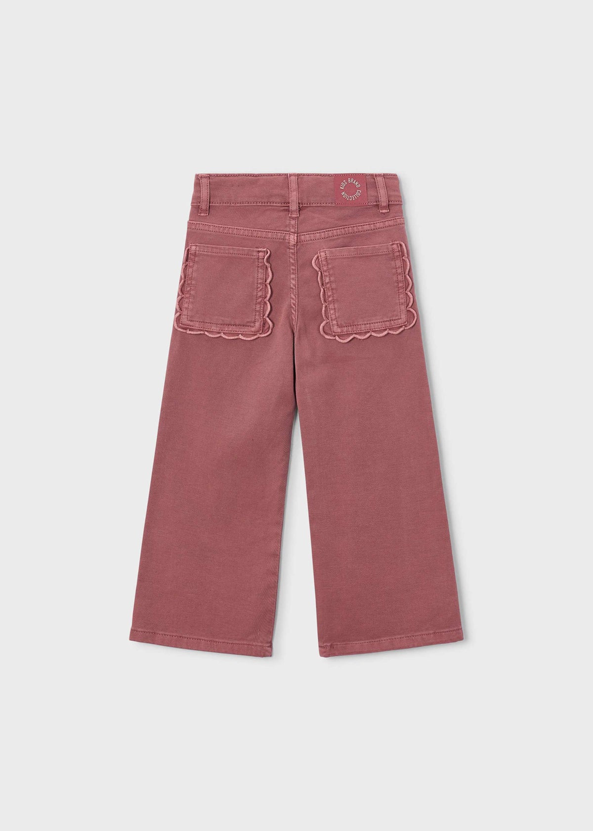 A pair of dusty rose cropped pants shown from the back, featuring scalloped edges on the back pockets and a small circular logo patch near the waistband, set against a light gray background.