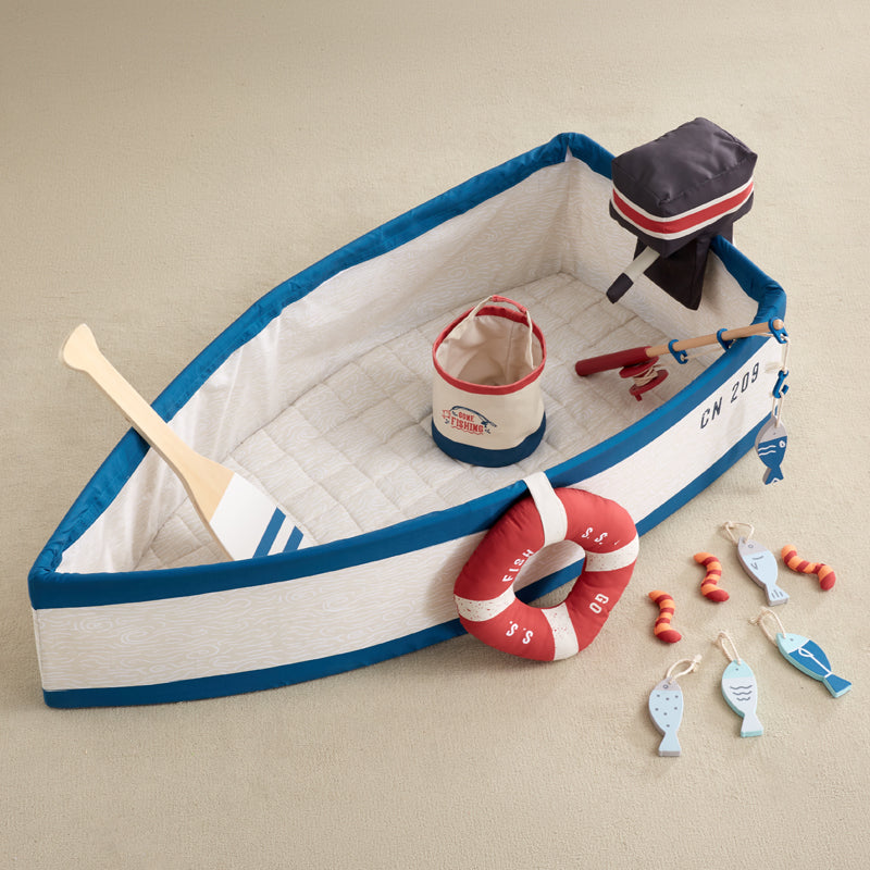A children's nautical-themed play boat set on a white background, featuring a fabric boat with blue and cream stripes, a red life preserver, a wooden paddle, and a small black motor attachment.