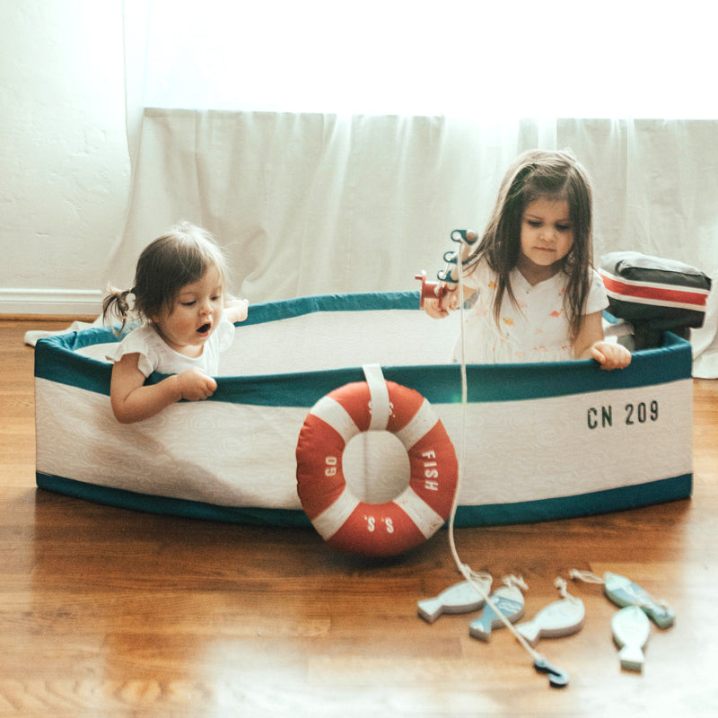 Two children playing with a toy boat on a wooden floor.