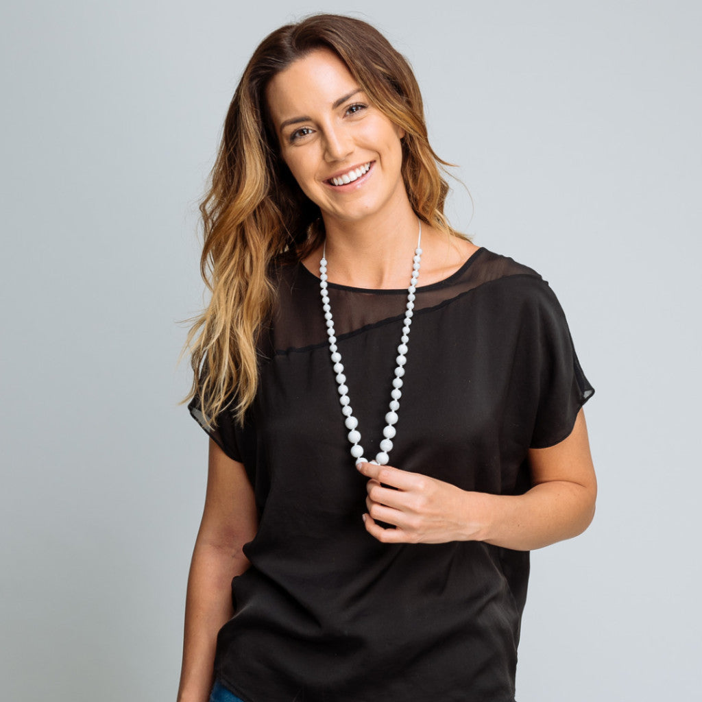 Woman wearing a black top and pearl necklace against a gray background