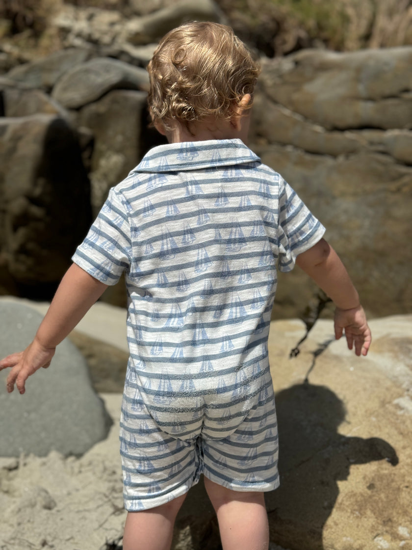 Child wearing a blue and white striped outfit standing on a rocky beach.