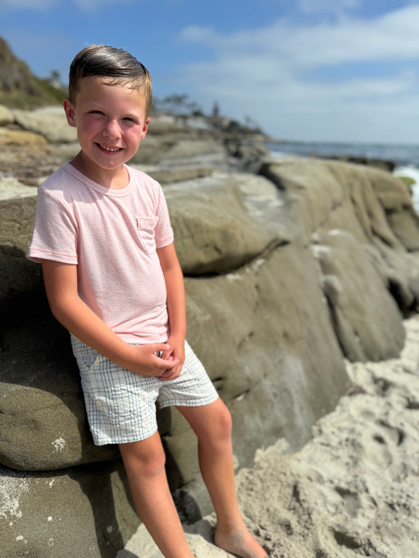 Young boy standing on a rocky beach with ocean and sky in the background