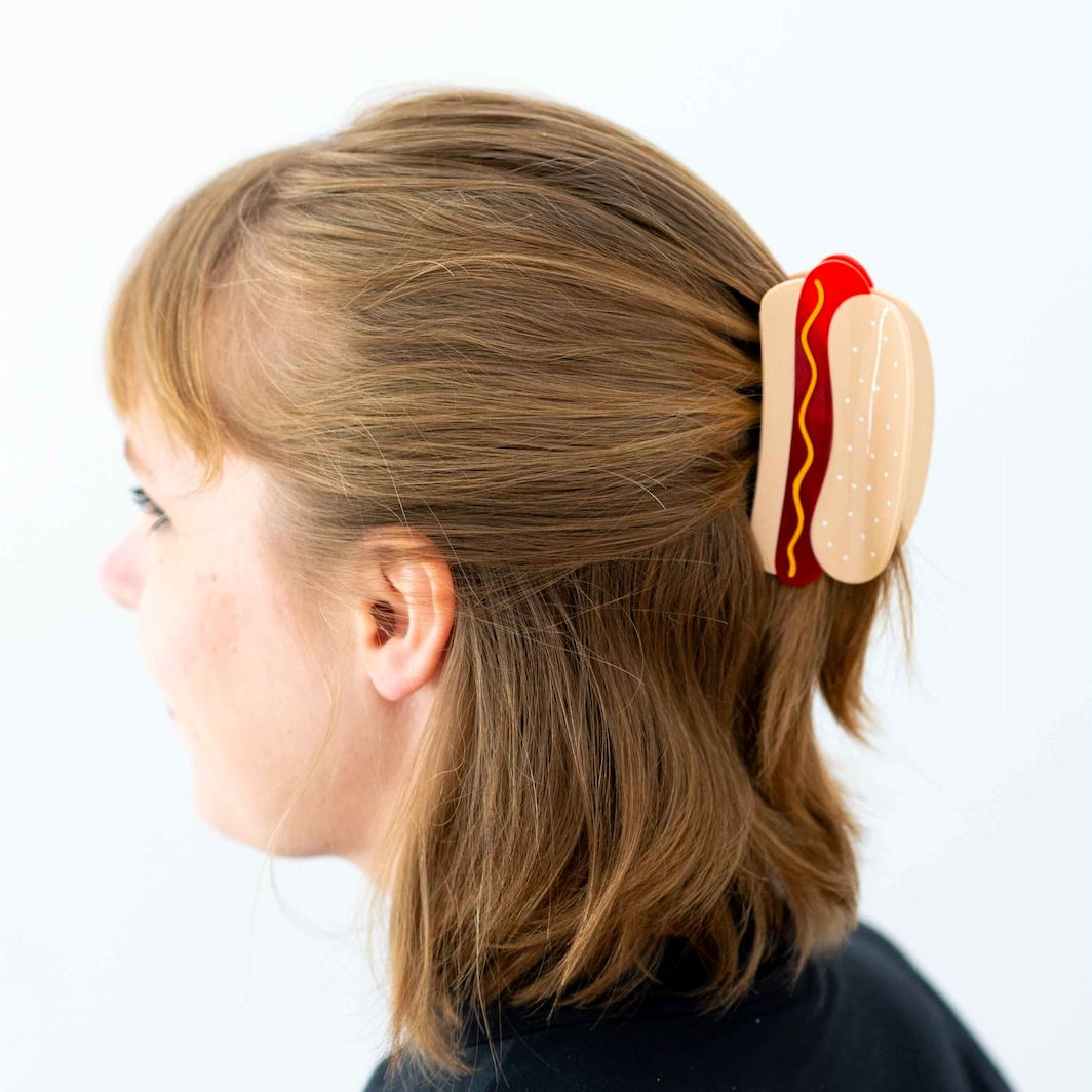 Person wearing a hot dog-shaped hair clip on a white background