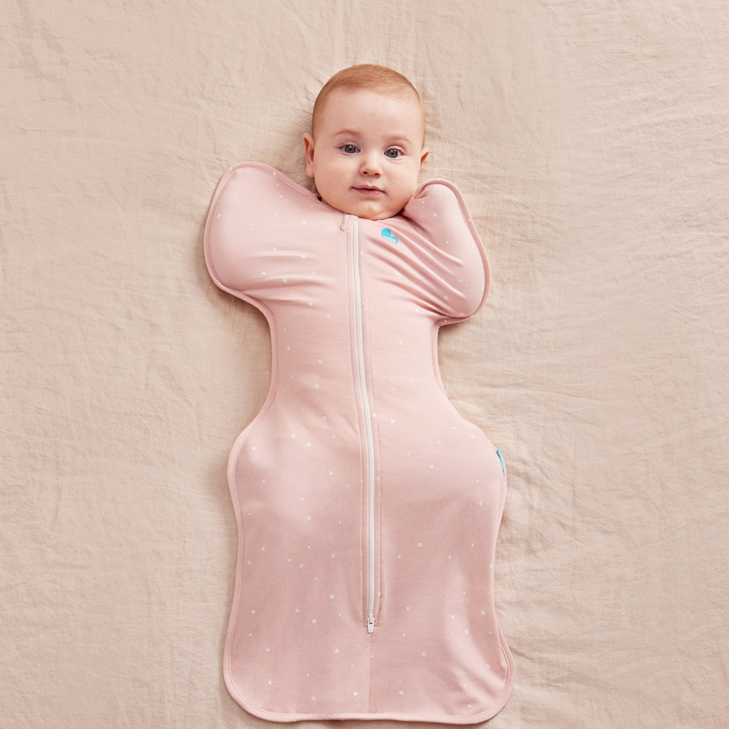Baby lying on a pink blanket wearing a pink swaddle with a zipper.