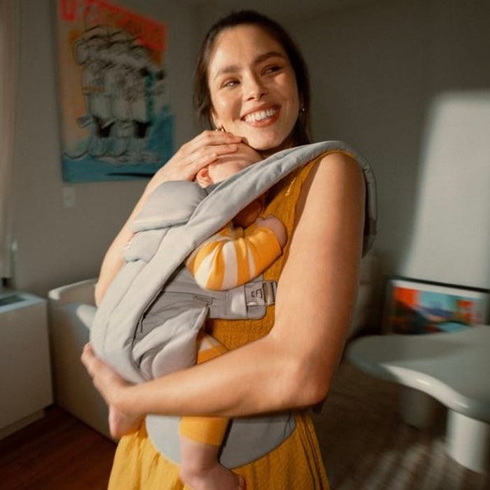 Woman smiling while holding a baby in a sling in a home setting