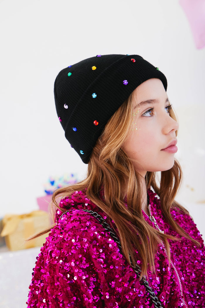 Person wearing a black beanie with colorful beads and a pink sequin jacket.