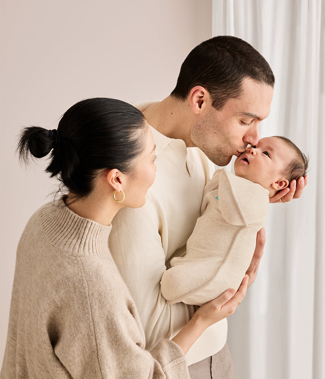 Man kissing a baby held by a woman, with a neutral background