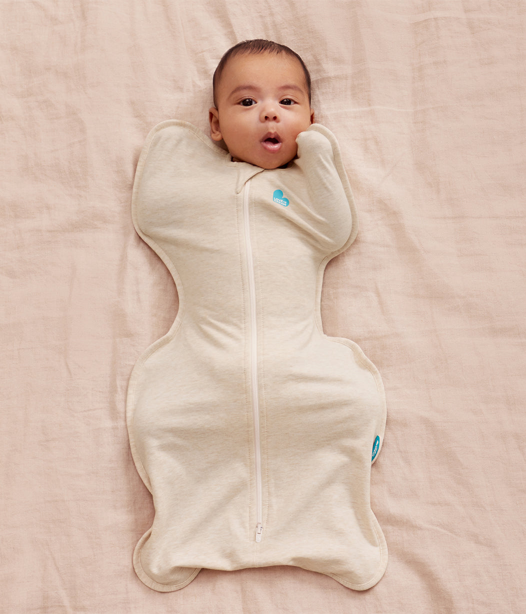 Baby wrapped in a cream-colored swaddle on a pink blanket