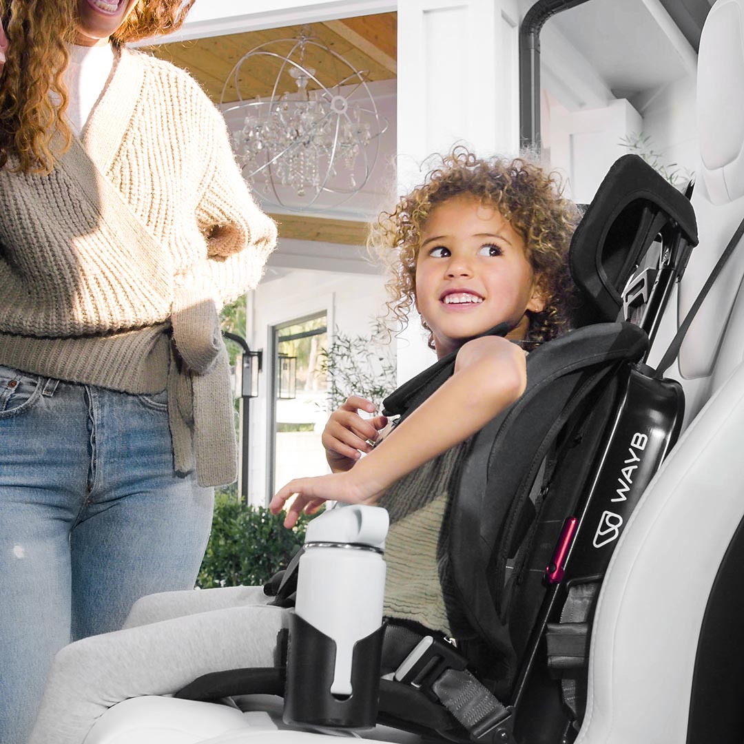 Child in a car seat with a woman standing nearby, inside a vehicle.