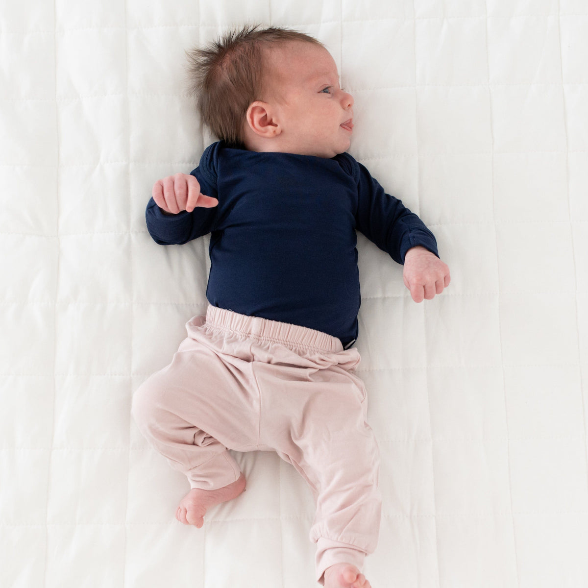 Baby lying on a white blanket wearing a navy blue onesie and pink pants.
