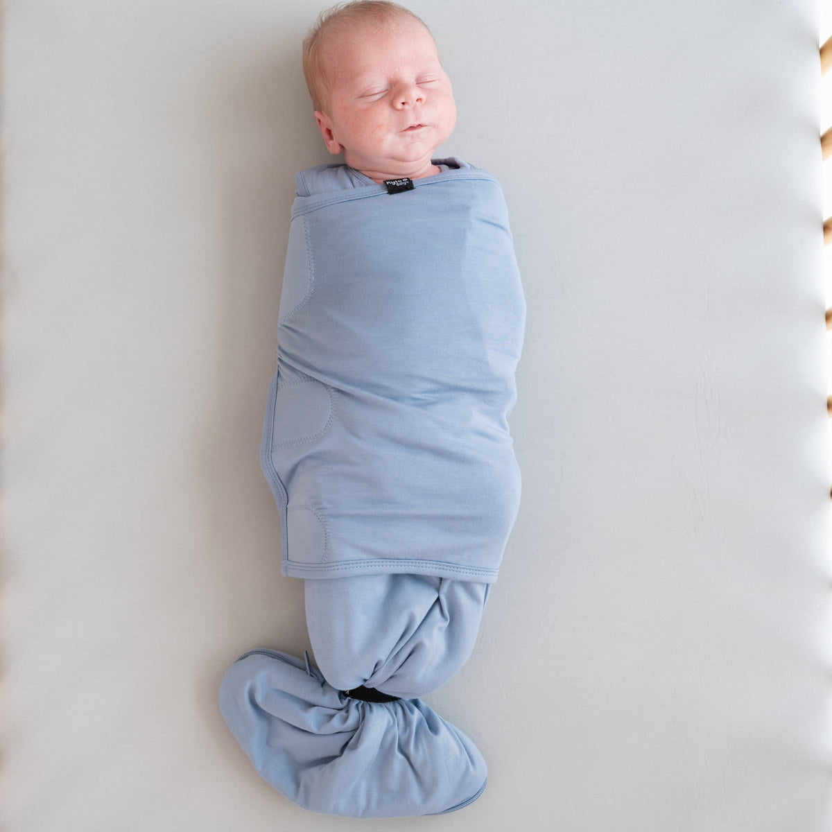 Newborn baby swaddled in a blue blanket on a light gray background