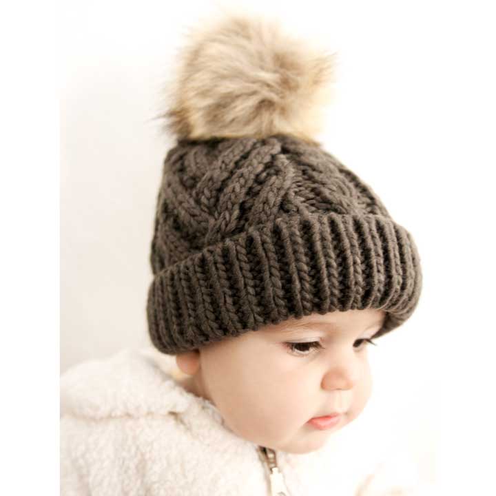 Knitted brown beanie with a fur pom-pom worn by a child on a white background