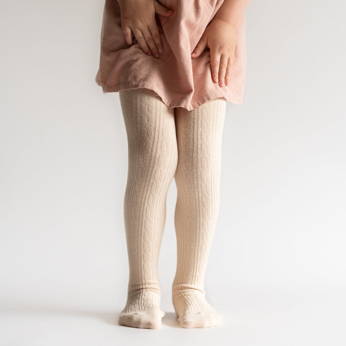 Person wearing beige tights and a pink dress on a plain background