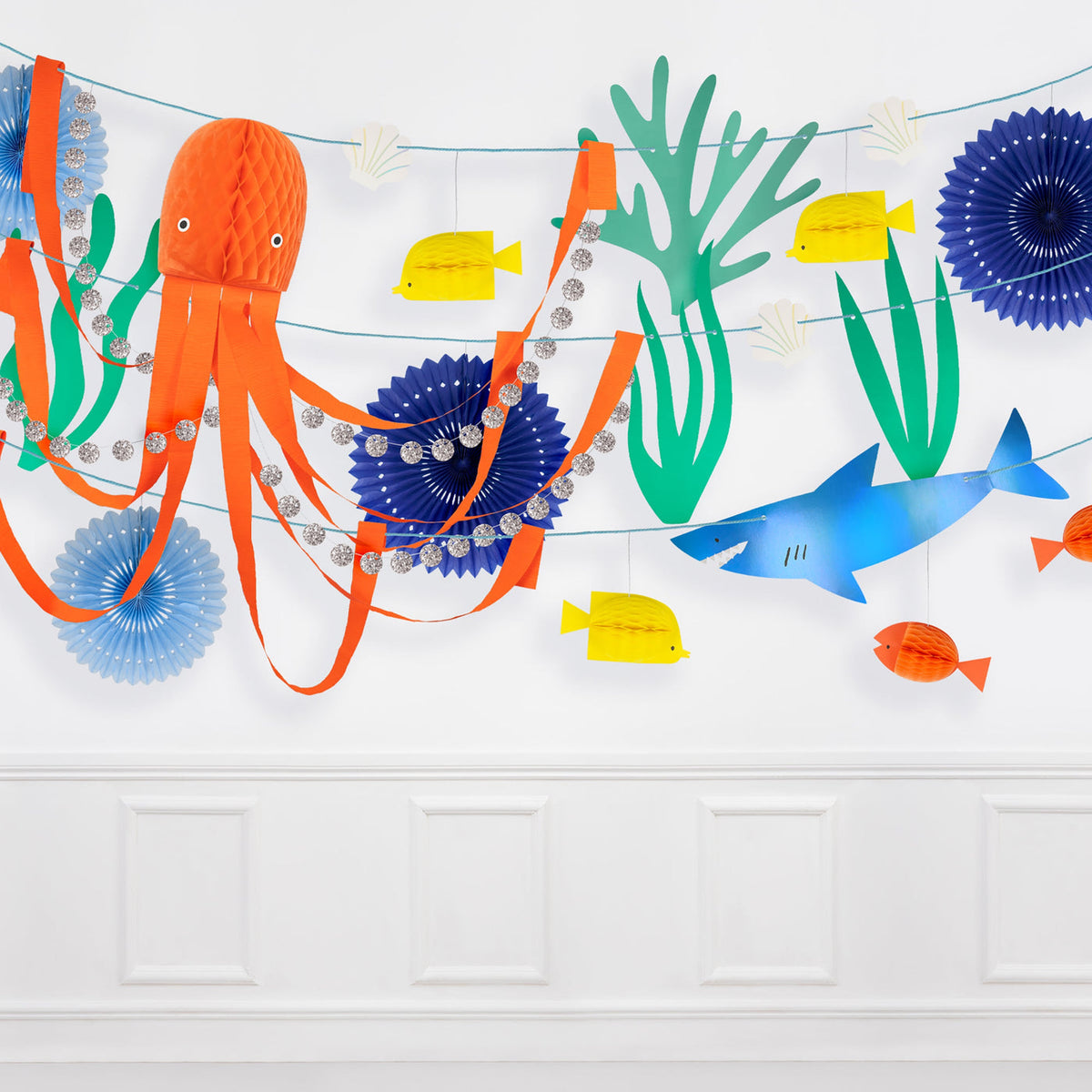 Colorful paper decorations of an octopus, fish, and plants on a white wall.