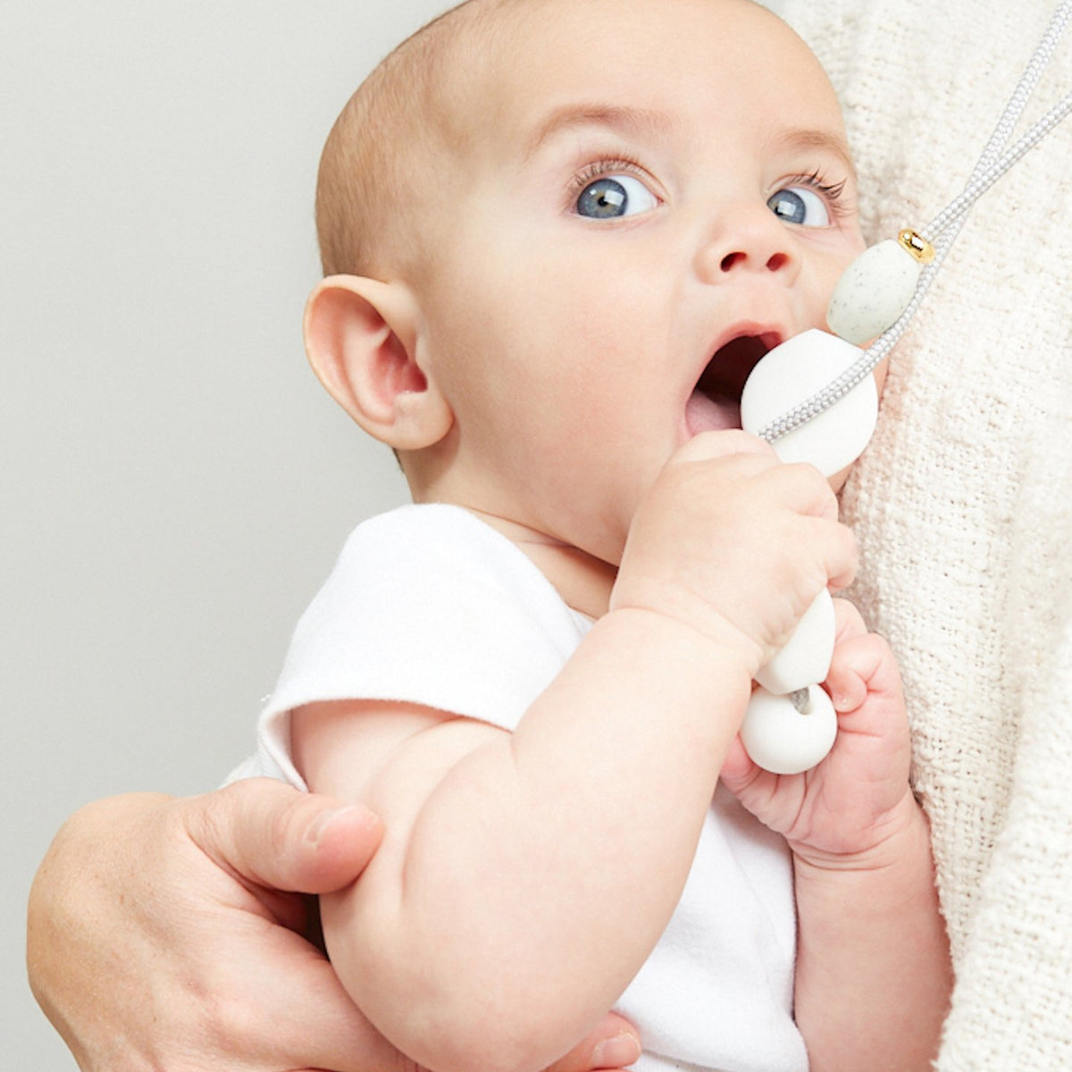 Baby holding a white toy with a neutral background