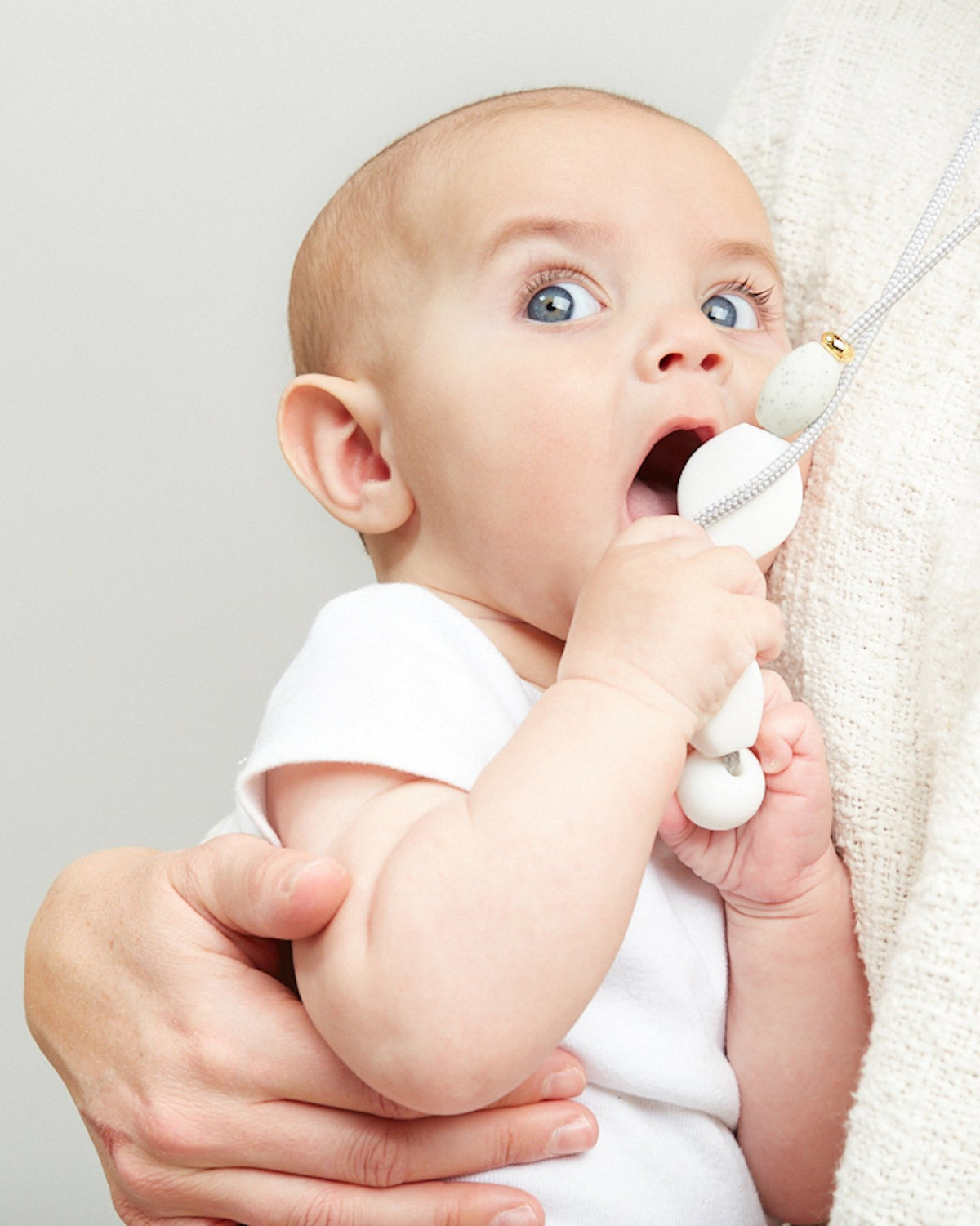 Baby holding a white toy with a neutral background