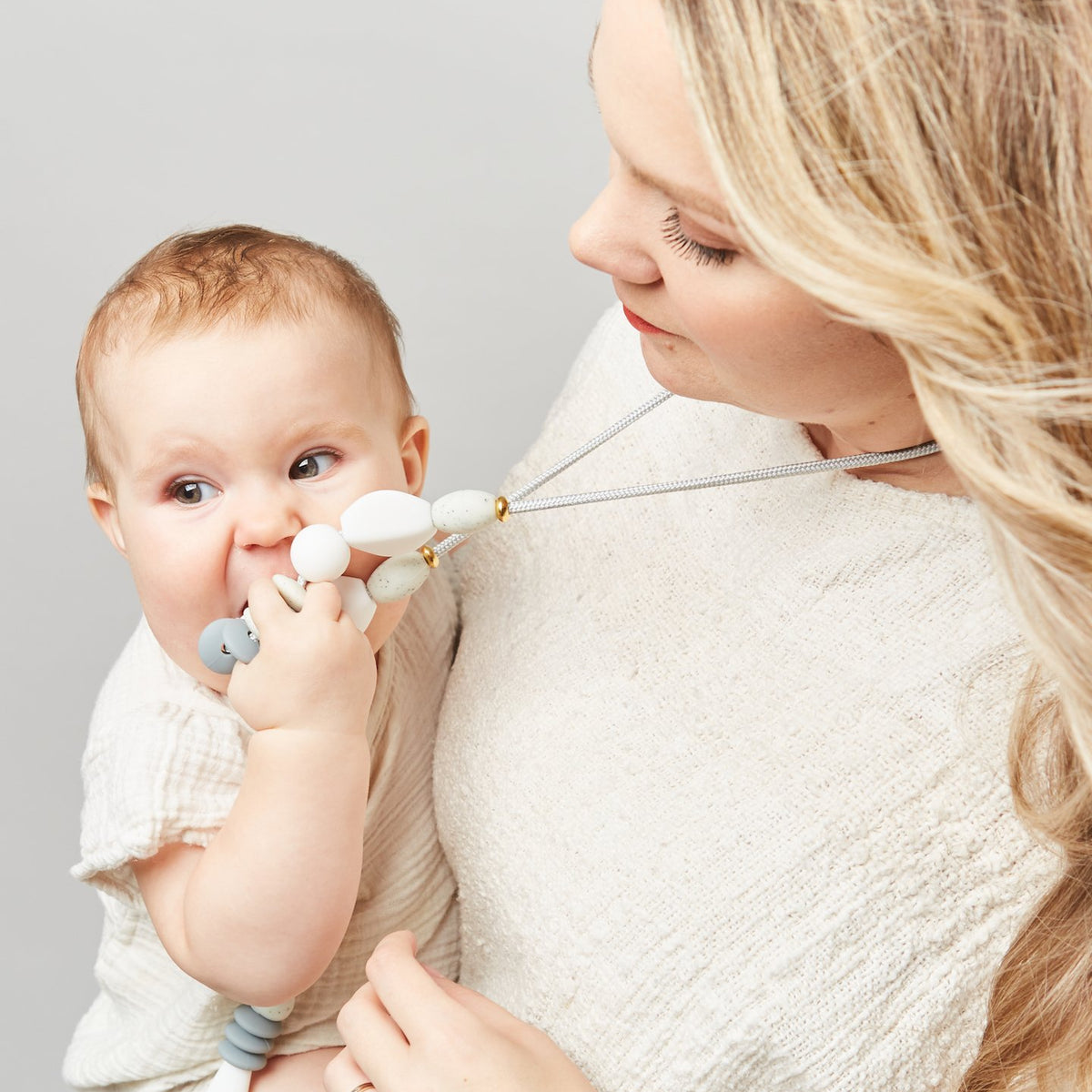 Woman holding a baby with a pacifier against a plain background