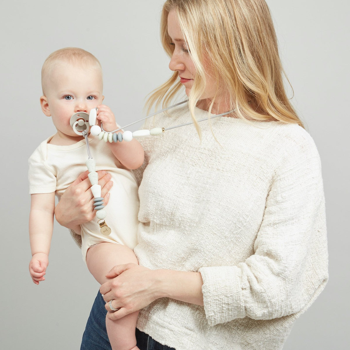 Woman holding a baby with a pacifier against a plain background