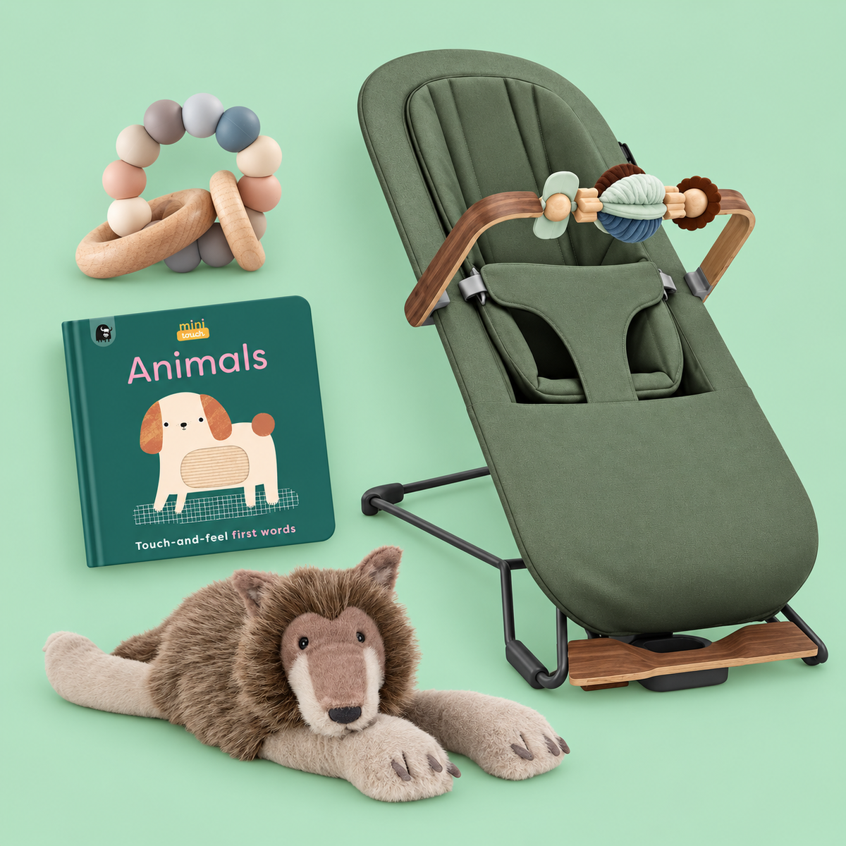 A baby care and toy set arranged on a pale mint background, including an olive green bouncer with wooden accents, a pastel bead teether, a green children's book titled 'Animals,' and a plush wolf toy.