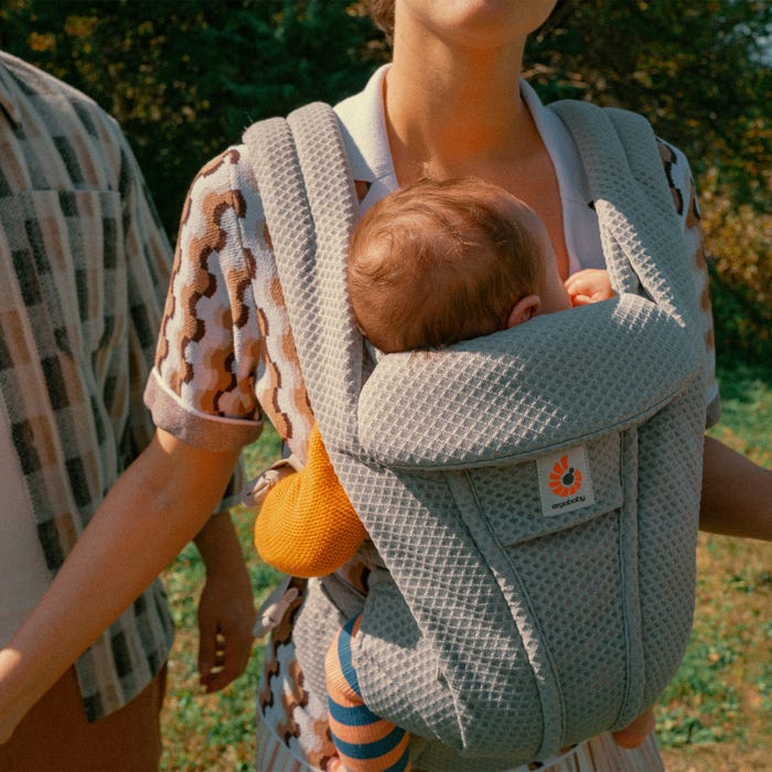 Person carrying a baby in a textured carrier outdoors.