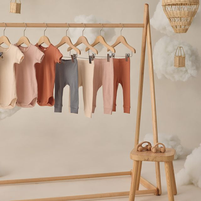 Children's leggings in various colors hanging on a wooden rack with a small wooden stool below.