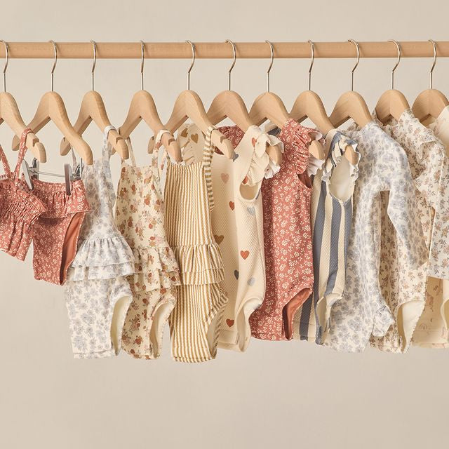 Row of baby clothes on hangers against a neutral background