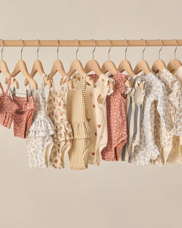 Row of baby clothes on hangers against a neutral background
