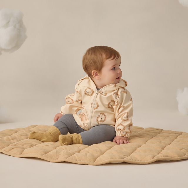 Baby in a beige quilted jacket sitting on a beige blanket against a neutral background