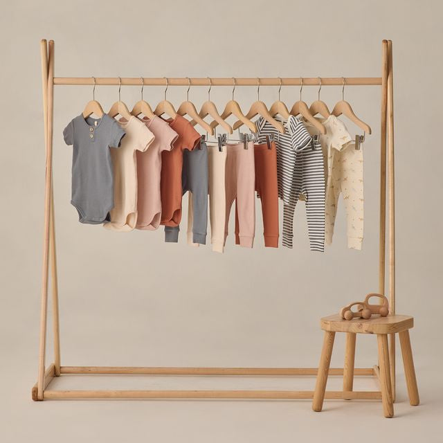 Wooden clothing rack with baby clothes on a beige background