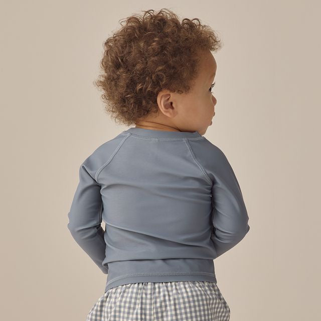 Child wearing a blue long-sleeve shirt and checkered pants on a beige background