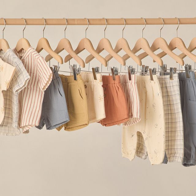 Row of children's clothing on wooden hangers against a beige wall