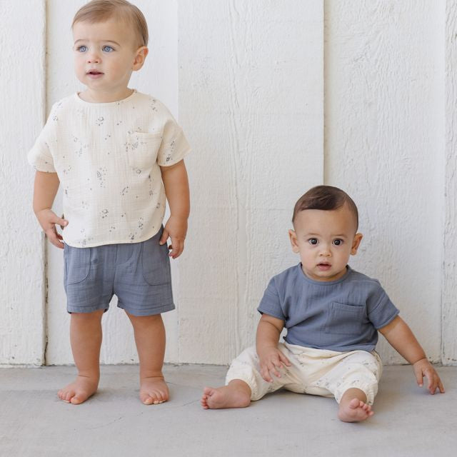 Two young children wearing matching outfits against a white wooden panel background