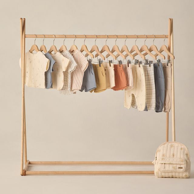 Wooden clothing rack with baby clothes on a beige background