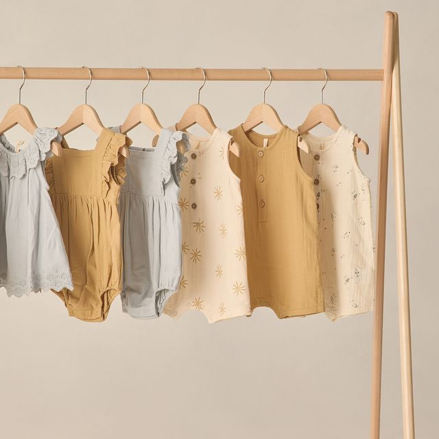 Set of baby rompers on hangers against a neutral background