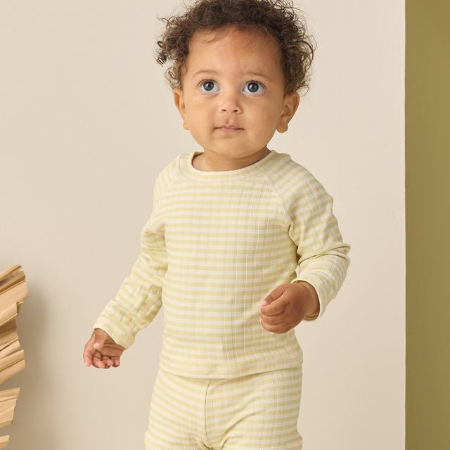 Baby wearing a yellow striped outfit standing against a beige background