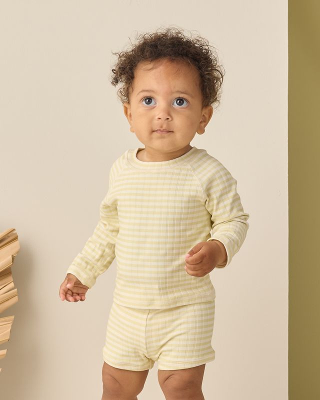 Baby wearing a yellow striped outfit standing against a beige background