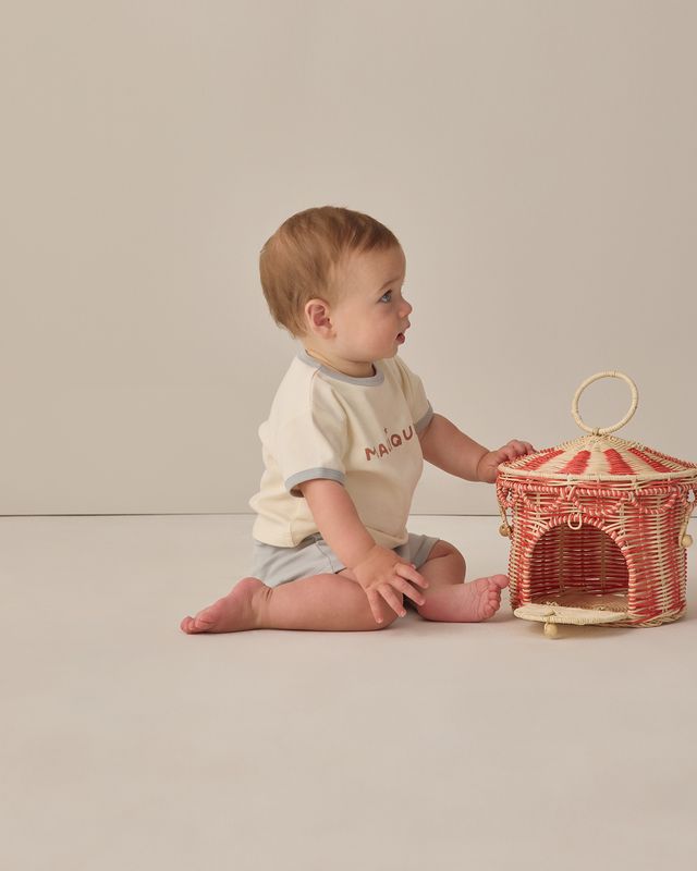 Baby playing with a small, decorative woven basket on a plain background