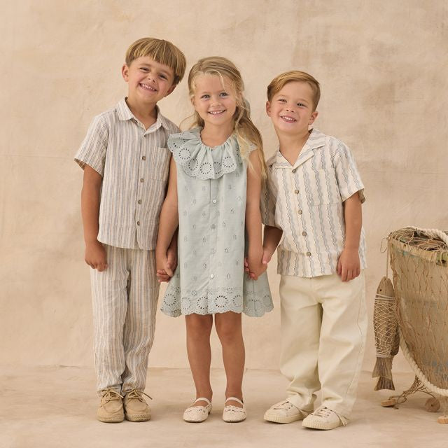 Three children in matching outfits standing together against a beige background
