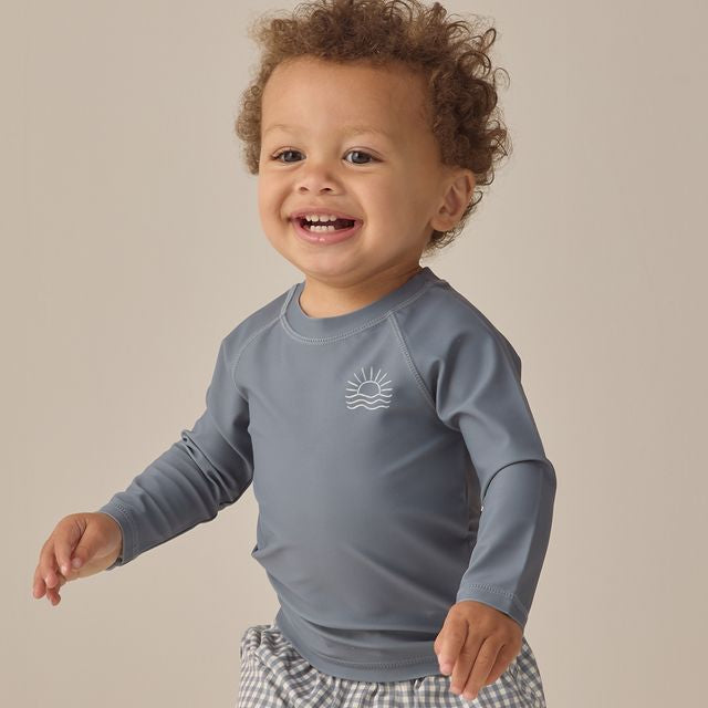 Child wearing a blue long-sleeve shirt with a logo on a beige background