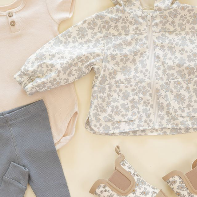 Children's clothing including a floral top, gray pants, and shoes on a light background