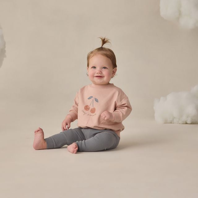 Child wearing a pink sweatshirt with a cherry design on a beige background