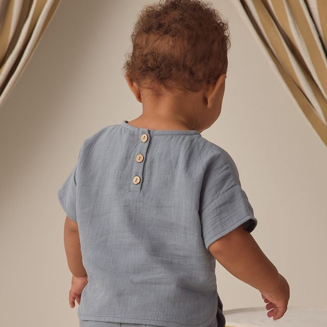 Child wearing a light blue shirt with buttons, standing against a neutral background