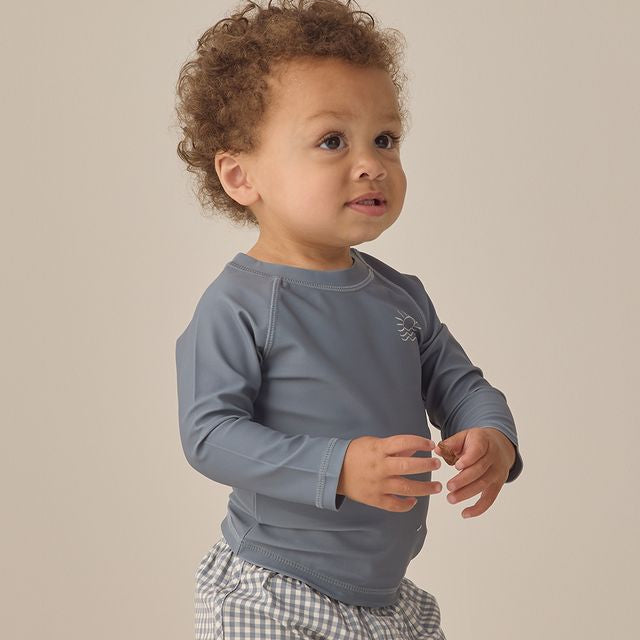 Child wearing a gray long-sleeve shirt and checkered shorts on a beige background