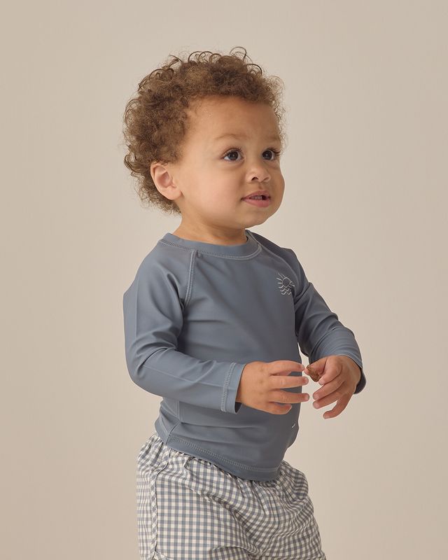 Child wearing a gray long-sleeve shirt and checkered shorts on a beige background