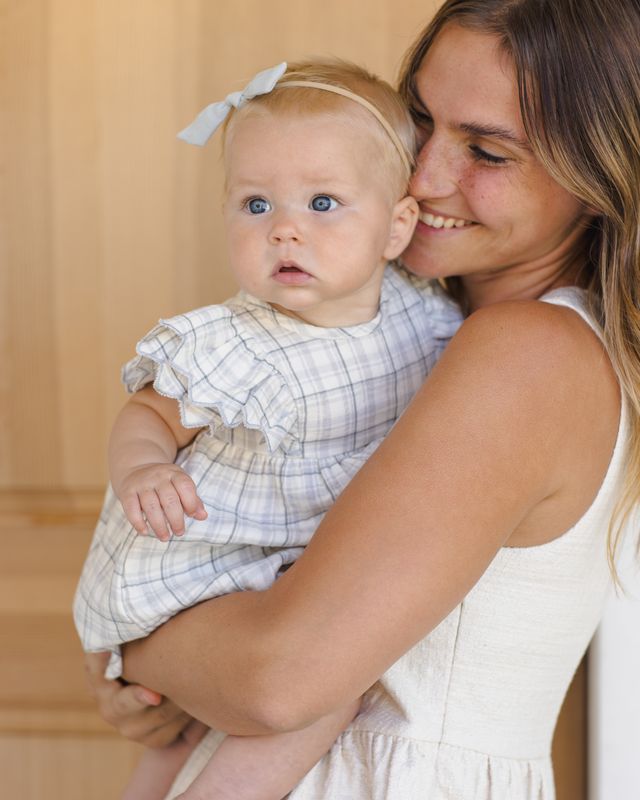 Woman holding a baby with a bow in her hair, both wearing white dresses.