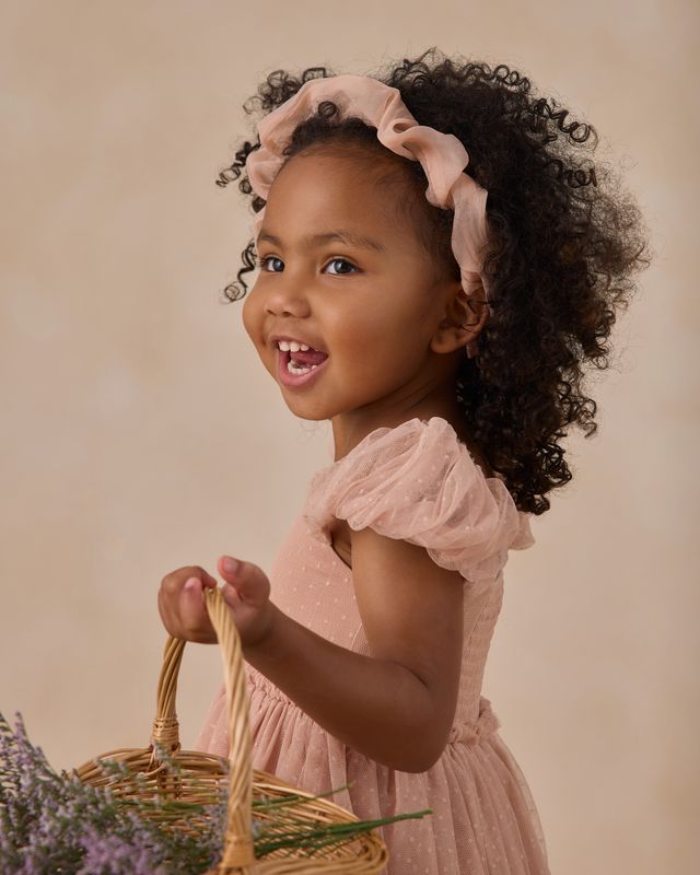 Young girl in a pink dress with a headband holding a wicker basket against a beige background